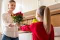 Happy Mother`s Day or Birthday Background. Adorable young girl surprising her mom with bouquet of red roses. Family celebration.