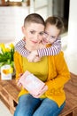 Happy Mother`s Day or Birthday Background. Adorable young girl surprising her mom, young cancer patient, with bouquet and present.