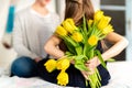 Happy Mother`s Day or Birthday Background. Unrecognizable young girl surprising her mom with bouquet of yellow tulips.