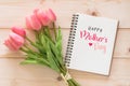 Happy MotherÃ¢â¬â¢s Day celebration greeting on white note book page background with tulip flower gift for mom on wood Royalty Free Stock Photo