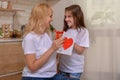 Happy mother`s day! Daughter Gives mom a gift box and a card with a heart at home on the background of the kitchen. Mum and girl Royalty Free Stock Photo