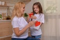 Happy mother`s day! Daughter Gives mom a gift box and a card with a heart at home on the background of the kitchen. Mum and girl Royalty Free Stock Photo