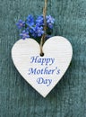 Happy Mother`s Day greeting card with decorative white heart and forget-me-not flowers on old blue wooden background. Royalty Free Stock Photo