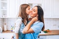 Happy Mother`s Day. Little daughter kissing and hugging her smiling mom in light modern kitchen together Royalty Free Stock Photo