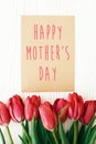 Happy Mother`s Day text and beautiful red tulips on white wooden background flat lay. Happy mother day greeting card with spring