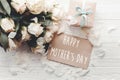 Happy Mother`s Day text sign on craft greeting card and white roses bouquet, gift box on wooden background, flat lay. Mothers day Royalty Free Stock Photo