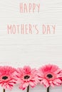 Happy Mother`s Day text sign at pink gerbera on white wooden background, flat lay. Floral greeting card. Mothers day. Pink Royalty Free Stock Photo