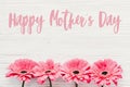 Happy Mother`s Day text sign at pink gerbera on white wooden background, flat lay. Floral greeting card. Mothers day. Pink Royalty Free Stock Photo