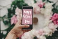 Happy Mother`s Day text sign on screen phone in hand at stylish pink and white peonies on pastel pink paper, flat lay. Stylish Royalty Free Stock Photo