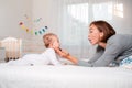 Happy Mother`s Day. A young mother plays with her baby on the bed. Side view. The concept of motherhood Royalty Free Stock Photo