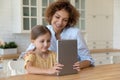 Happy mother and small girl use tablet computer at kitchen