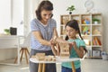 Happy mother and smiling daughter sitting on floor and looking at wooden pyramid at home