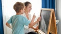 Happy mother with smiling son learning and writing alpabet on blackboard with chalks at home Royalty Free Stock Photo