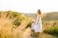 Happy mother and son are walking in picturesque field at sunset.