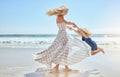 Happy mother swinging and spinning cute daughter in circles by the arms at the beach. Playful, energetic and joyful kid