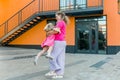 Happy mother swinging and spinning cute daughter in circles by the arms outdoors. Playful energetic and joyful kid