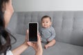 Happy mother taking a picture of her baby girl on sofa with smart phone Royalty Free Stock Photo