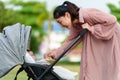 happy mother talking and playing with her infant baby in the stroller while resting in park