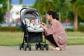 happy mother talking and playing with her infant baby in the stroller while resting in park