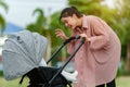 happy mother talking and playing with her infant baby in the stroller while resting in park