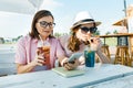 Happy mother and teen daughter talking and smiling. Parents with a kid in a summer outdoor cafe enjoying cold drinks on a hot