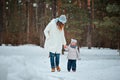 Happy mother and toddler daughter walking in winter snowy forest