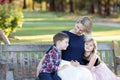 Happy mother with two children sitting on a wooden bench in a garden Royalty Free Stock Photo