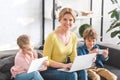 happy mother using laptop and smiling at camera while kids using digital devices Royalty Free Stock Photo