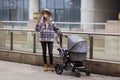 Happy Mother walking With Stroller In Park and using mobile phone. Joy of motherhood. Stylish young caucasian woman Royalty Free Stock Photo