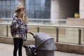 Happy Mother walking With Stroller In Park and using mobile phone. Joy of motherhood. Stylish young caucasian woman Royalty Free Stock Photo