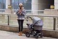 Happy Mother walking With Stroller In Park and using mobile phone. Joy of motherhood. Stylish young caucasian woman Royalty Free Stock Photo