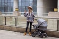 Happy Mother walking With Stroller In Park and using mobile phone. Joy of motherhood. Stylish young caucasian woman Royalty Free Stock Photo