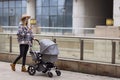 Happy Mother walking With Stroller In Park and using mobile phone. Joy of motherhood. Stylish young caucasian woman Royalty Free Stock Photo