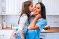 Happy Mother& x27;s Day. Little daughter kissing and hugging her smiling mom in light modern kitchen together Royalty Free Stock Photo