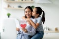 Happy mother& x27;s day. Little girl greeting her mom with gift card with big red heart and kissing mommy in cheek Royalty Free Stock Photo