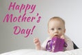 Happy mothers day. Adorable little baby lying on the white blanket and holding purple gift bag in his hands. Horisontal studio sho Royalty Free Stock Photo
