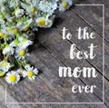 Happy mothers or womens day greeting card with field camomiles over dark grey rustic wooden background and white brush text Royalty Free Stock Photo