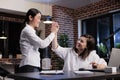 Happy motivated businesswomen in office workspace celebrating successful business deal by highfiving each other. Royalty Free Stock Photo