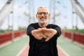 Happy well-fit senior sportsman exercising on city bridge, stretching hands Royalty Free Stock Photo