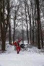Happy motorcyclist in a Santa Claus suit shows likes. Winter forest with falling snow. Touring motorcycle in the background. The