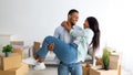 Happy moving day. Loving african american couple celebrating relocation, husband lifting his wife up on hands, panorama Royalty Free Stock Photo