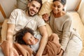 Happy multi ethnic family mom, dad and child laughing, playing and tickles in bed at home