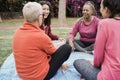 Happy multi generational women having fun together sitting outdoors at city park - Focus on african senior face