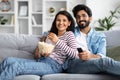 Happy multicultural couple watching TV at home, eating popcorn Royalty Free Stock Photo