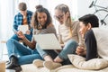 happy multicultural teens looking at laptop and sitting