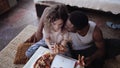 Happy multiethnic couple sitting on the flow, hugging and eating fast food. Woman feed the hungry man a slice of pizza. Royalty Free Stock Photo