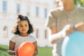 Happy multiethnic different age kids play with balloons outdoor in summer. Curly cute hispanic girl inflate, be measured