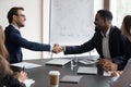 Happy multiethnic diverse business leaders shaking hands over meeting table