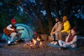Happy multiethnic friends having fun playing music and enjoying bonfire camping in nature at night