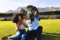 Happy multiracial children cuddling cheerful parents from behind sitting on grassy field in yard Royalty Free Stock Photo
